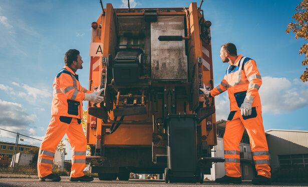 Two refuse collection workers loading garbage into waste truck
